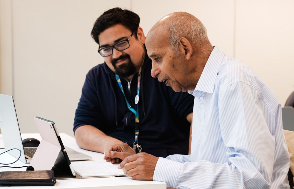 An elderly male customer and a male library worker interact at a library digital learning session.